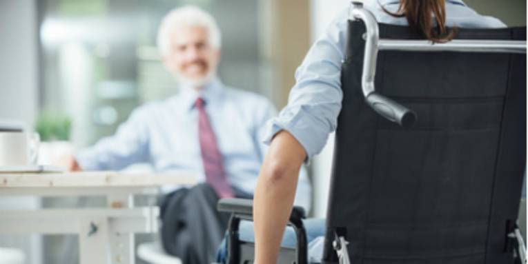 eine Person sitzt mit dem Rücken zur Kamera in einem Rollstuhl, im Hintergrund sieht man eine verschwommene Person zur Person gerichtet sitzen.