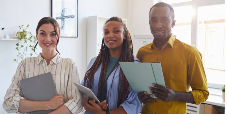 Drei Personen lächeln in die Kamera und halten jeweils ein iPad und Ordner.